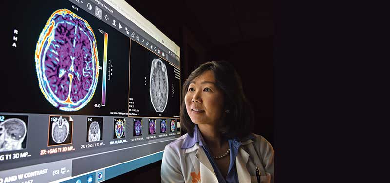 Michelle Kim, MD stands in front of brain scans